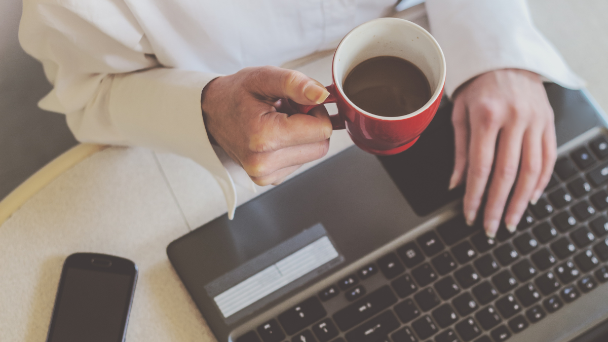 Personne utilisant un ordinateur, avec un café à la main