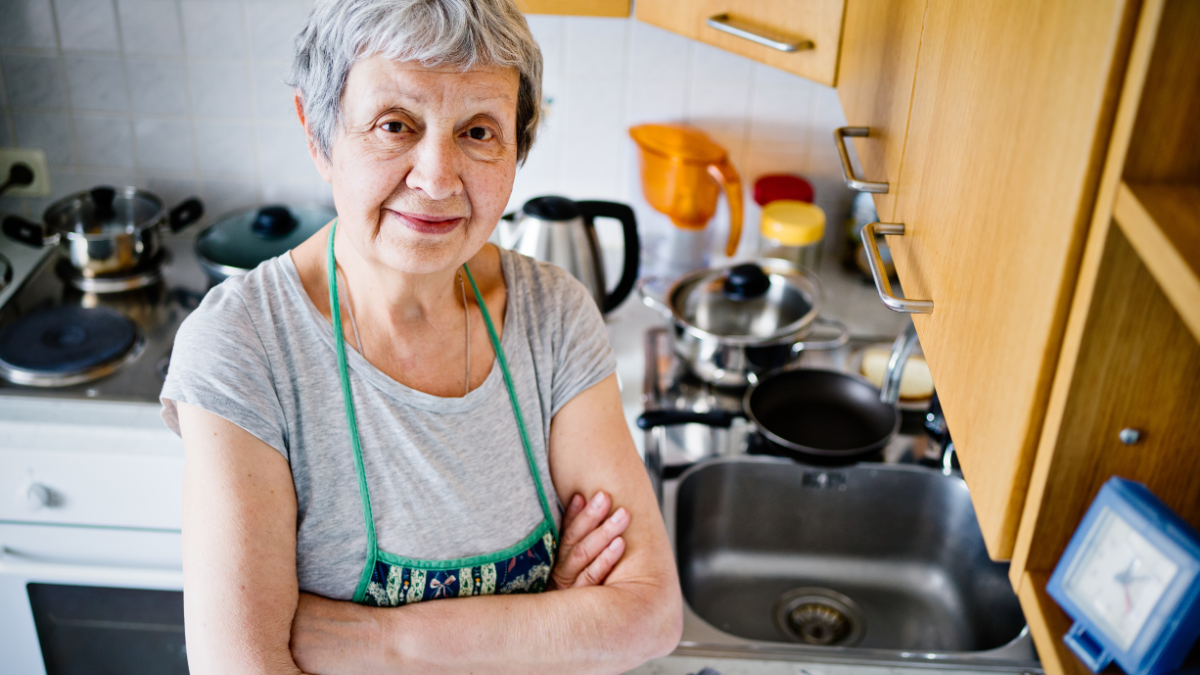 Dame âgée, souriante qui regarde l'objectif depuis sa cuisine